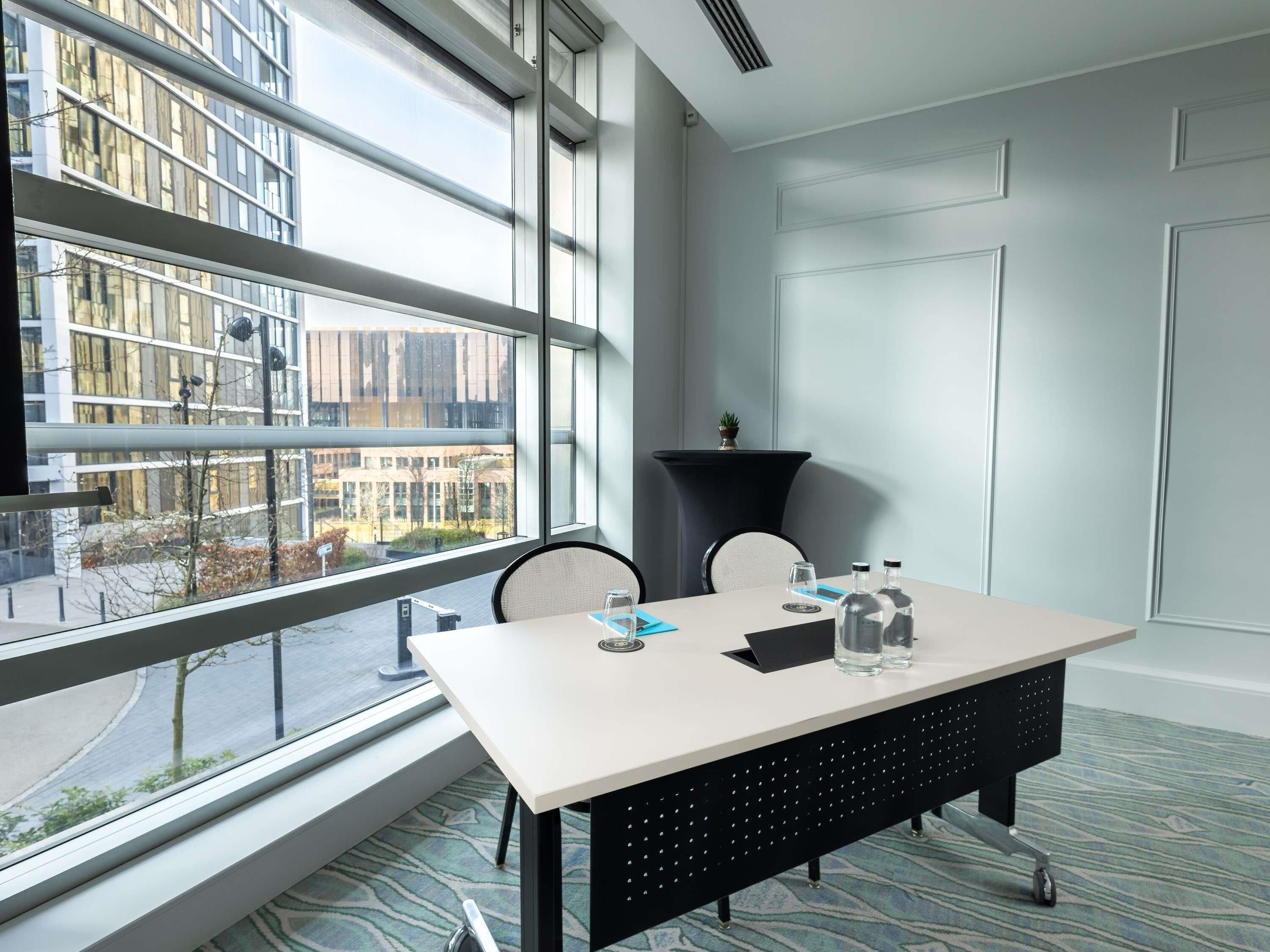 A modern conference room with a large window, a table with chairs, and a small potted plant.