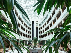 Un atrium à plusieurs niveaux, doté d’une colonne centrale, et entouré d’espaces aménagés avec des sièges et des plantes.