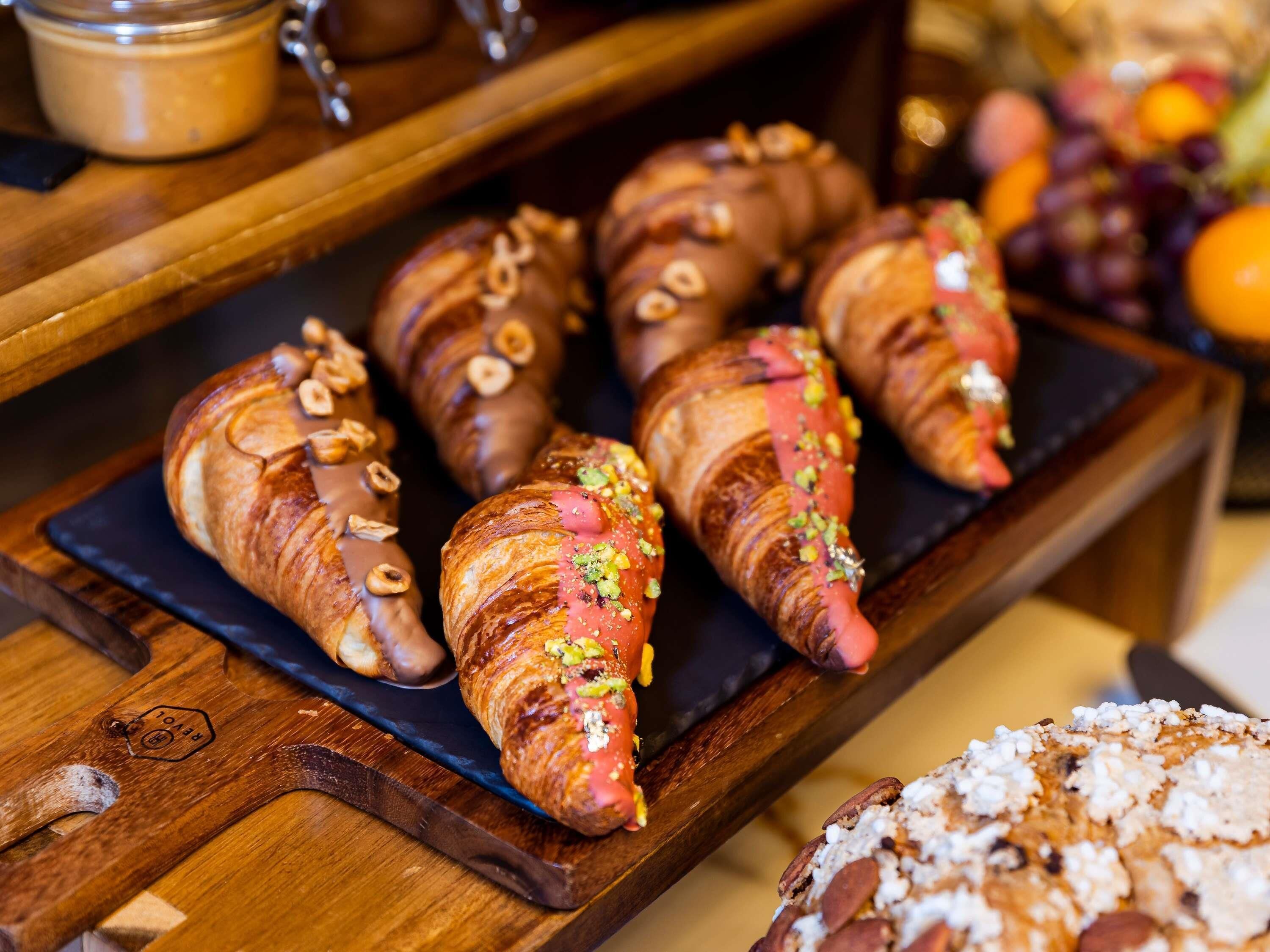 A wooden serving board with croissants and a pastry.