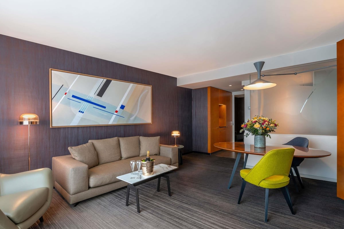 Une chambre d’hôtel moderne, dotée d’un canapé, d’une table à manger avec des chaises, d’une table basse et d’un grand tableau abstrait accroché au mur.