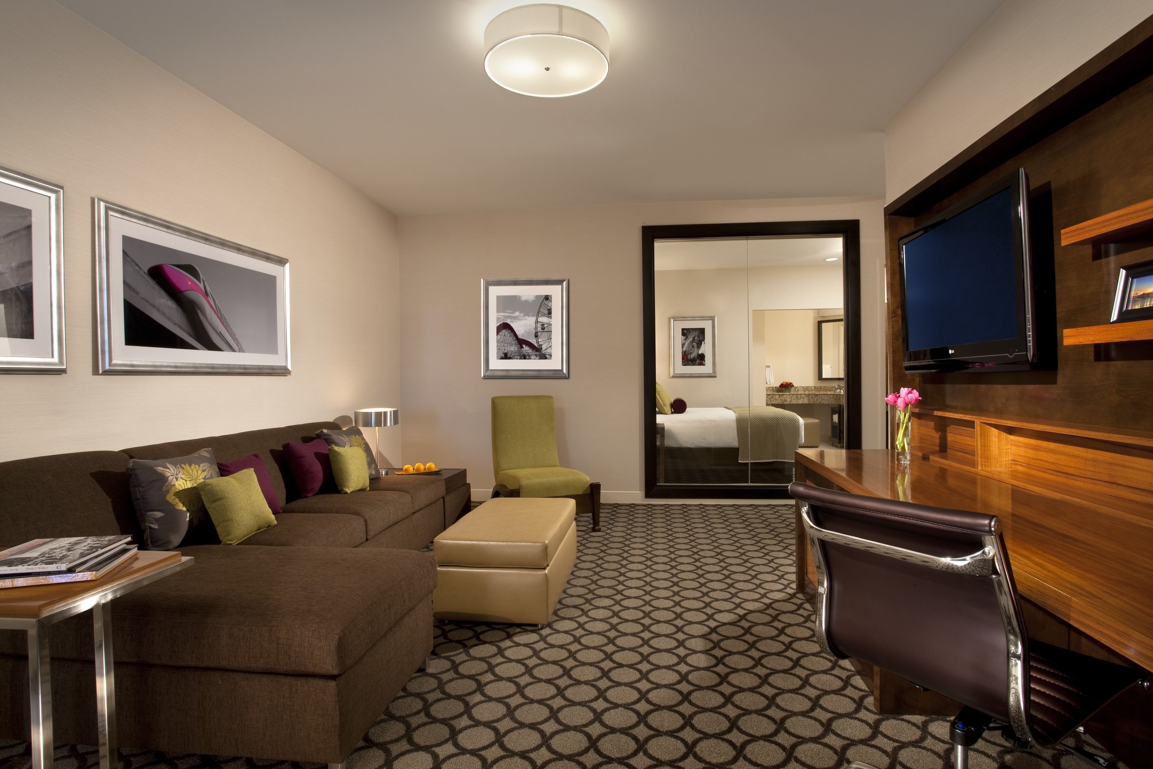 Een hotelkamer met een bruine bank, een groene fauteuil, een houten bureau, een televisie en ingelijste foto's aan de muren.