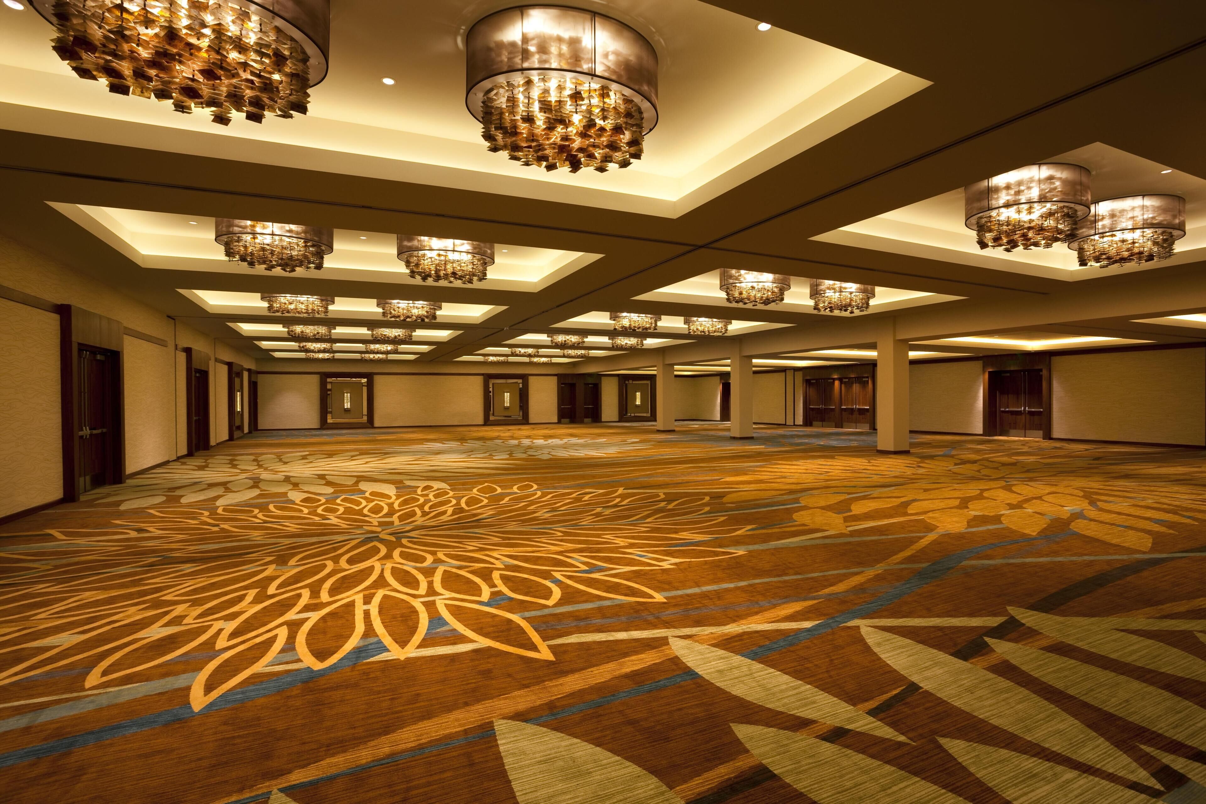 A large, well-lit conference room with a patterned carpet, multiple chandeliers, and a symmetrical ceiling design.