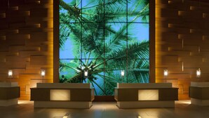 A reception area with a large wall mural of palm trees, two reception desks, and wall-mounted lights.