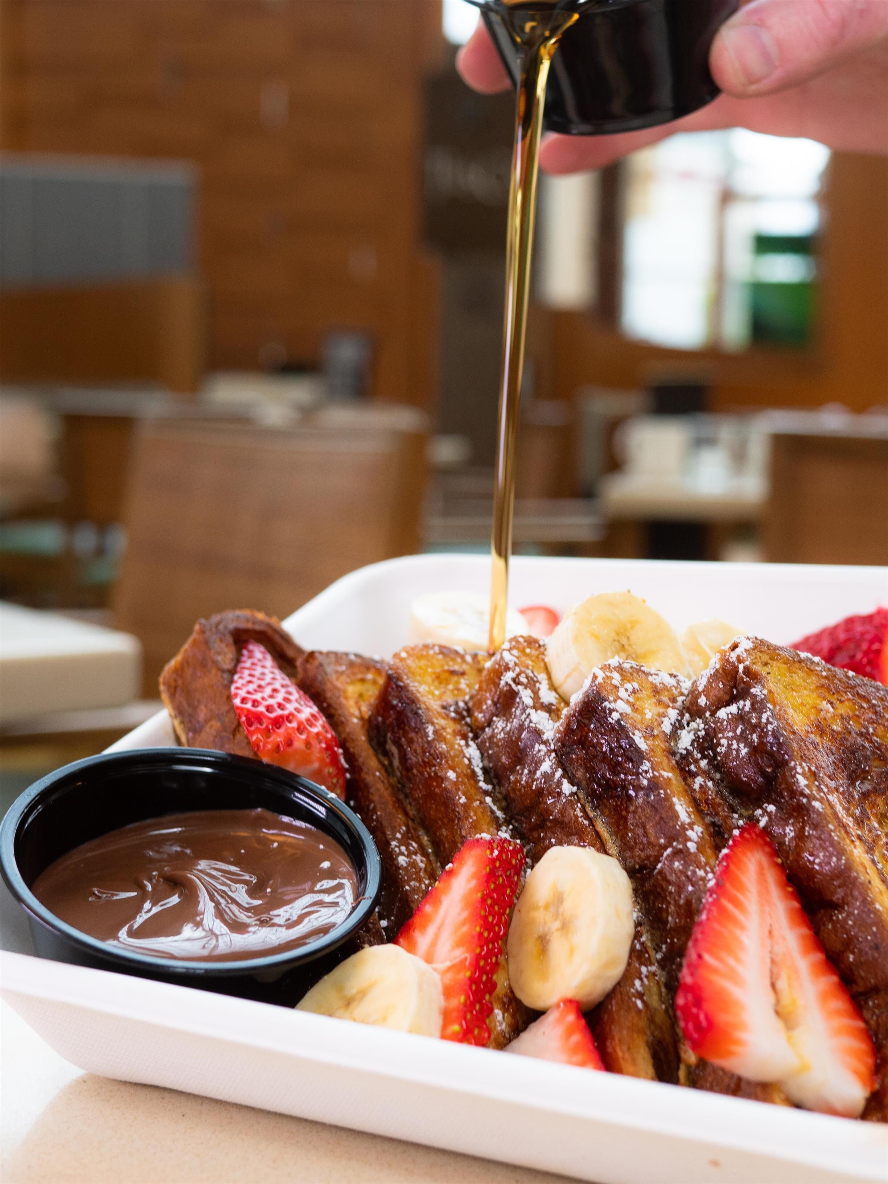 Une assiette de petit-déjeuner comprenant des tranches de pain perdu, des fraises, des bananes et une sauce au chocolat.