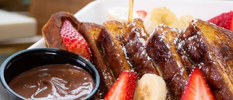 A breakfast plate with French toast, strawberries, bananas, and chocolate sauce.