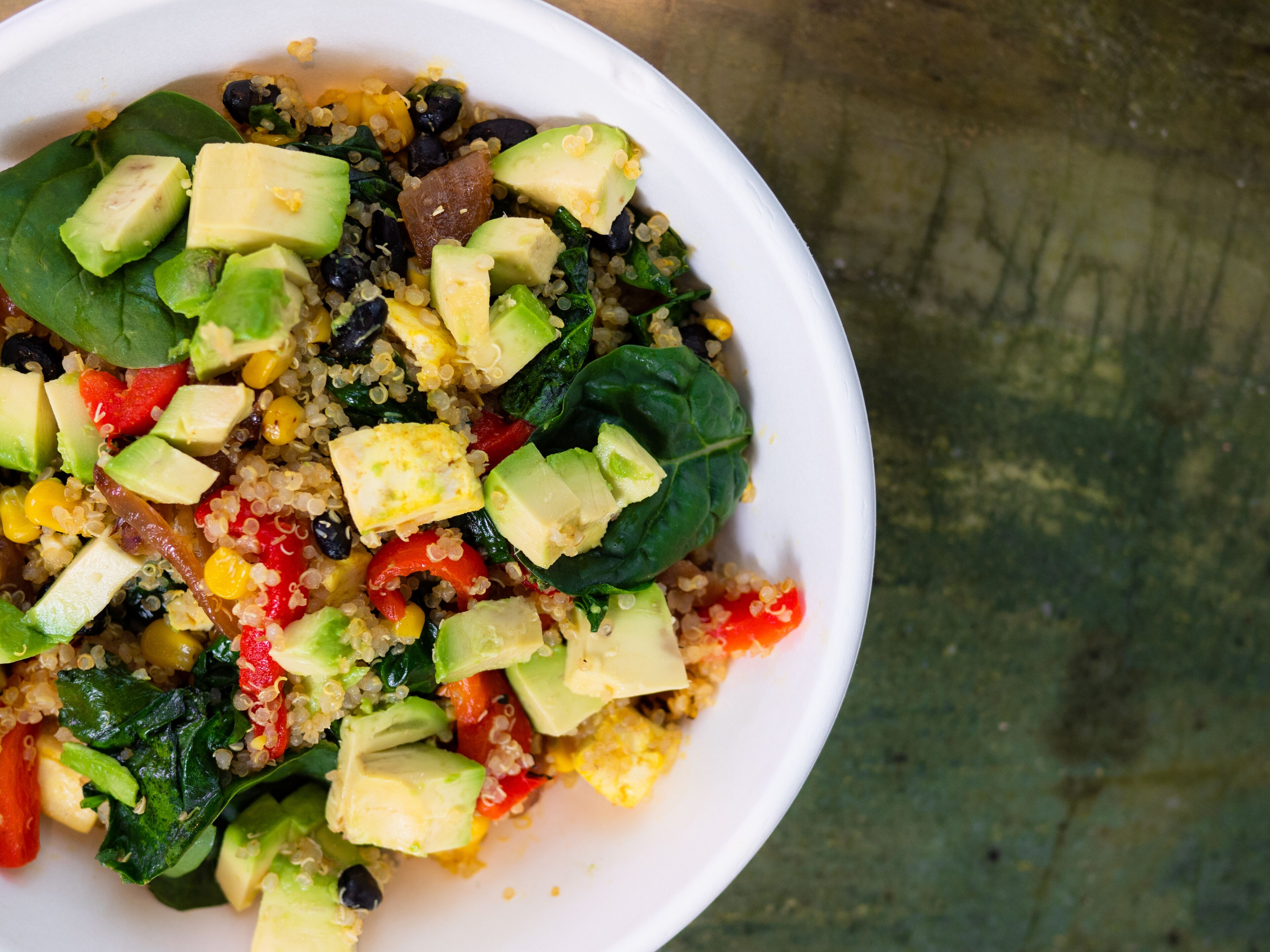 A bowl of quinoa salad with avocado, corn, and spinach.