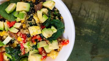 A bowl of quinoa salad with avocado, corn, and spinach.