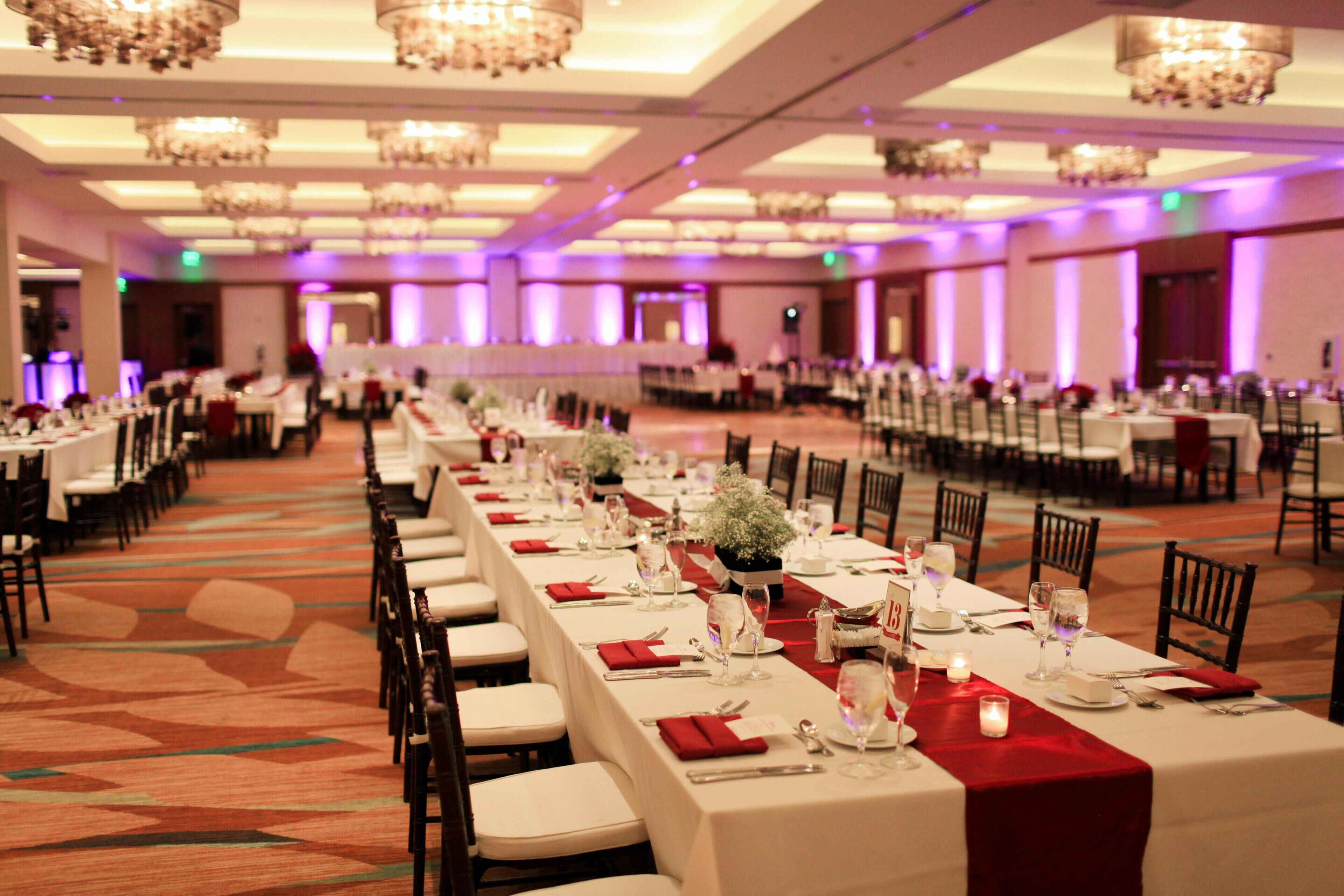 A banquet hall with long tables, chairs, chandeliers, and a carpeted floor.