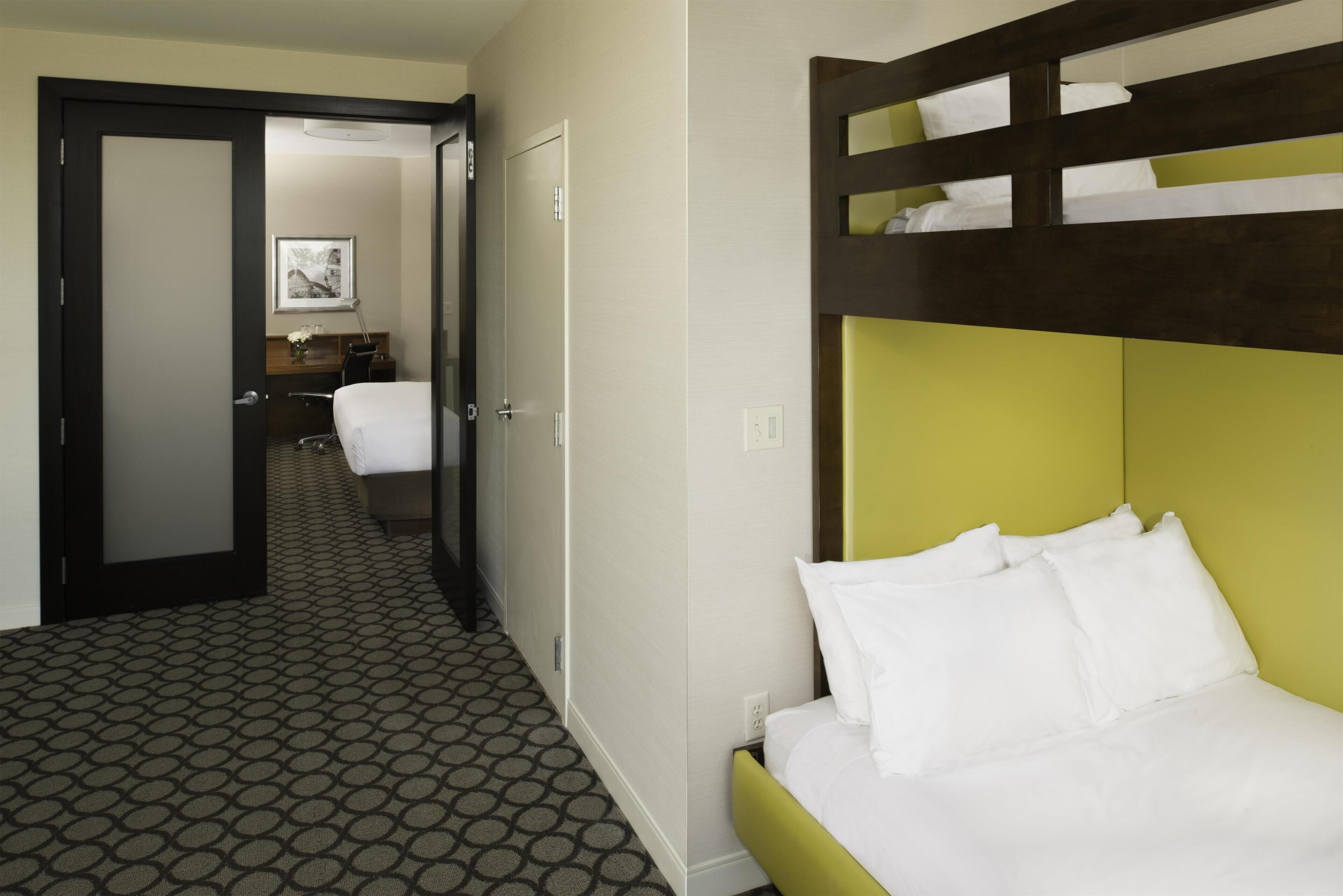 Habitación de hotel con literas, baño con toallero y pasillo que conduce a otra habitación.