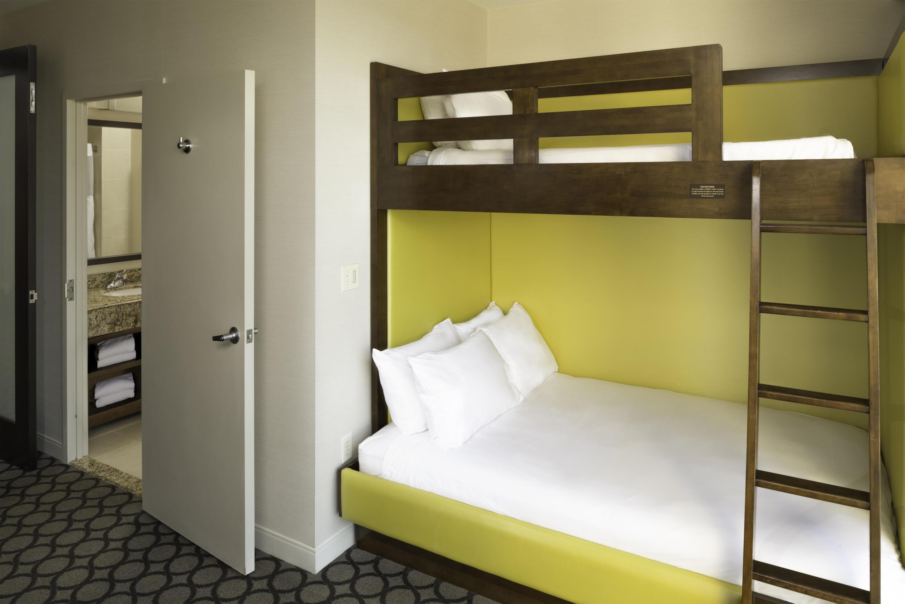 Uma cama de beliche com cabeceira verde, colchão branco e escada de madeira.