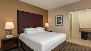 A hotel room with a large bed, two bedside tables with lamps, a framed picture on the wall, and a bathroom visible through an open door.