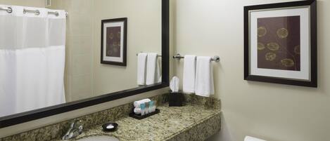 A bathroom with a granite countertop, a sink, a toilet, a shower curtain, a framed picture, and a towel rack.