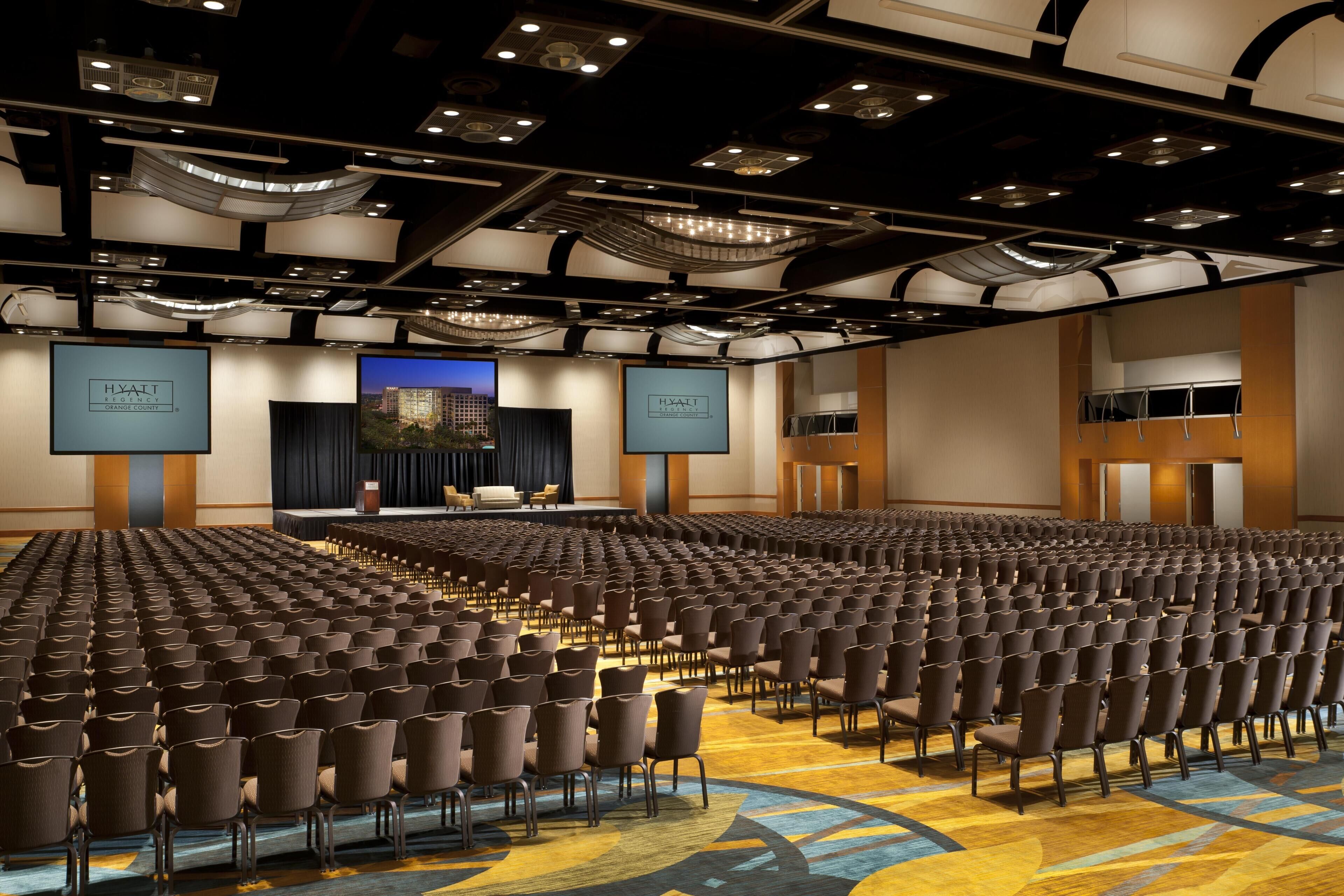 A large conference room with rows of chairs, a stage with a screen, and a 'HYATT' sign.
