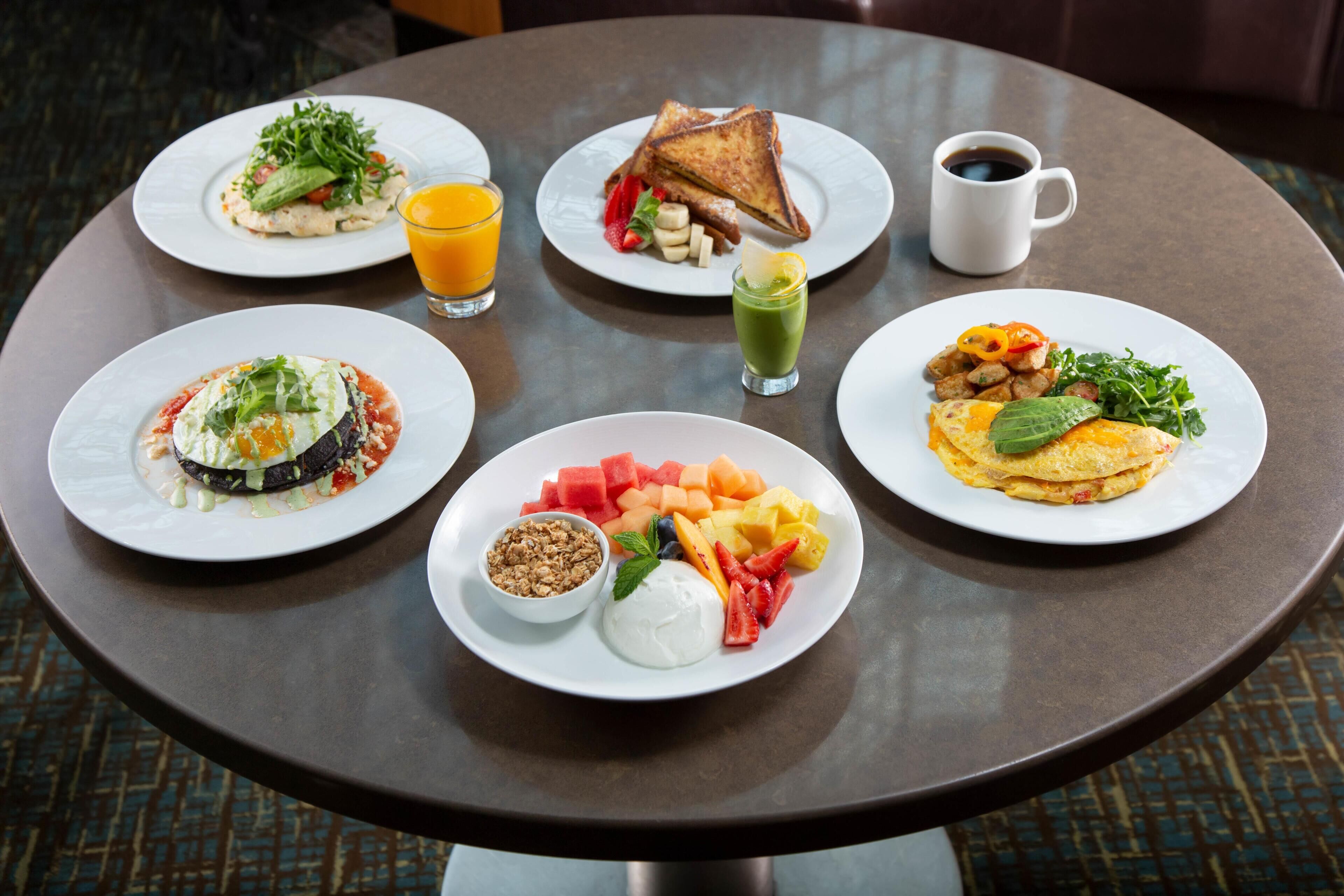 A table with various breakfast dishes, including toast, fruit, and a green drink.