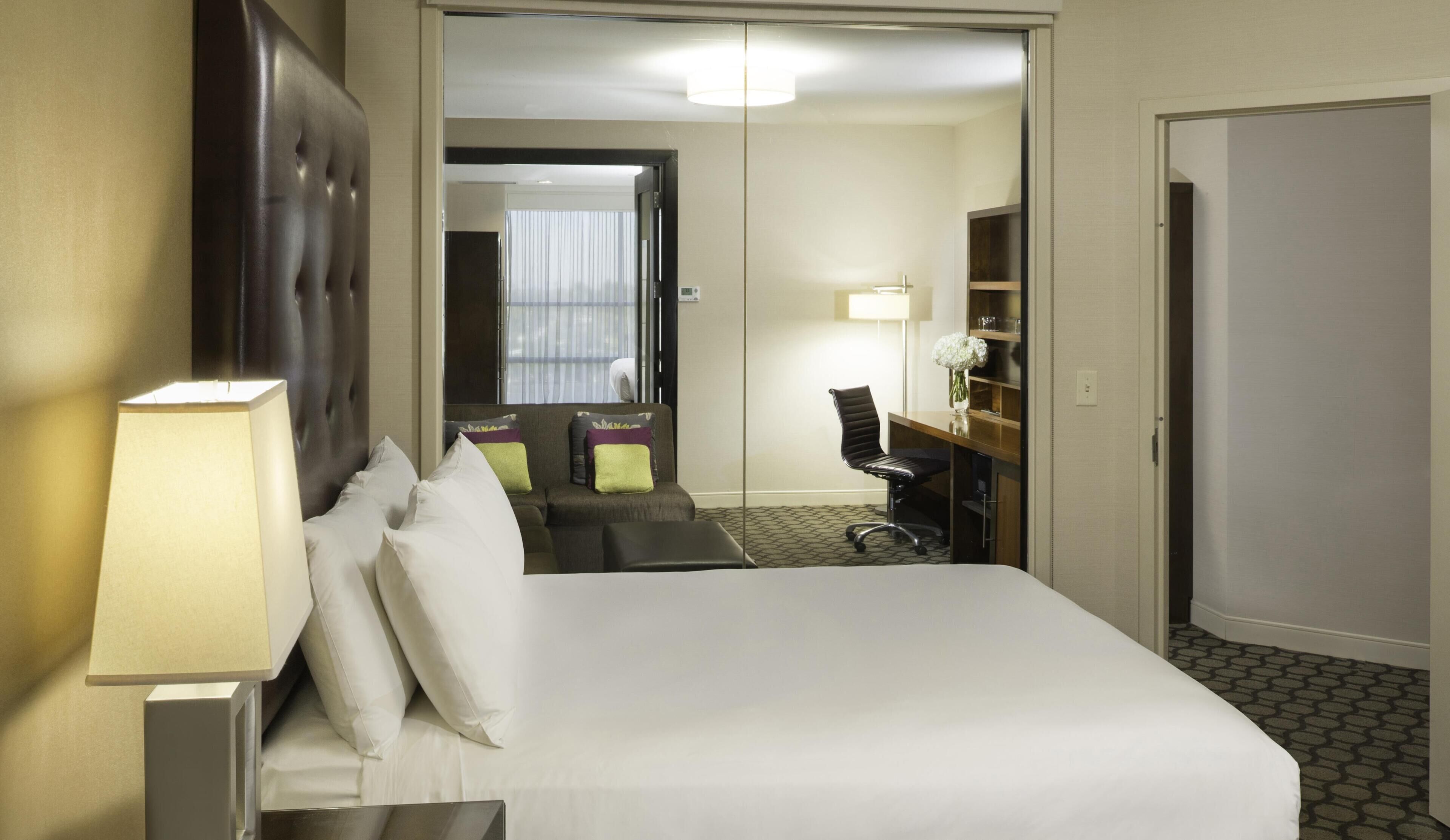 A hotel room with a bed, a desk, a chair, a lamp, and a mirror.