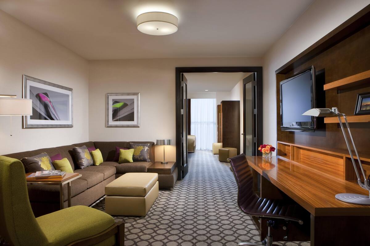 A hotel room with a sofa, armchair, desk, and TV.