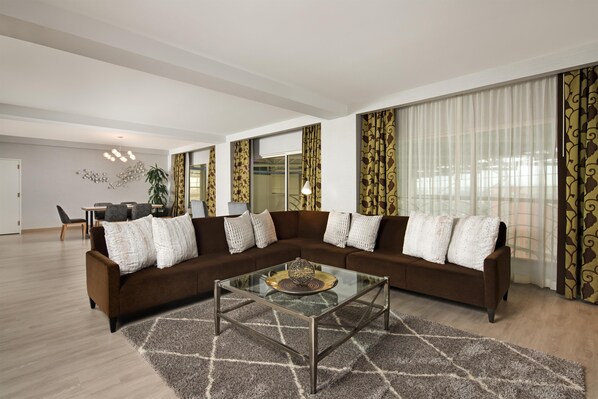 A modern living room with a sectional sofa, a glass coffee table, and a dining area in the background.