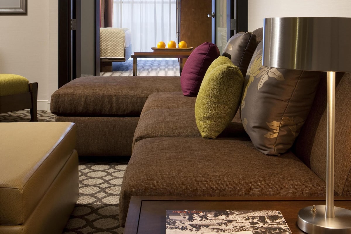 A modern living room with a brown sectional sofa, a small table with a book, and a lamp.