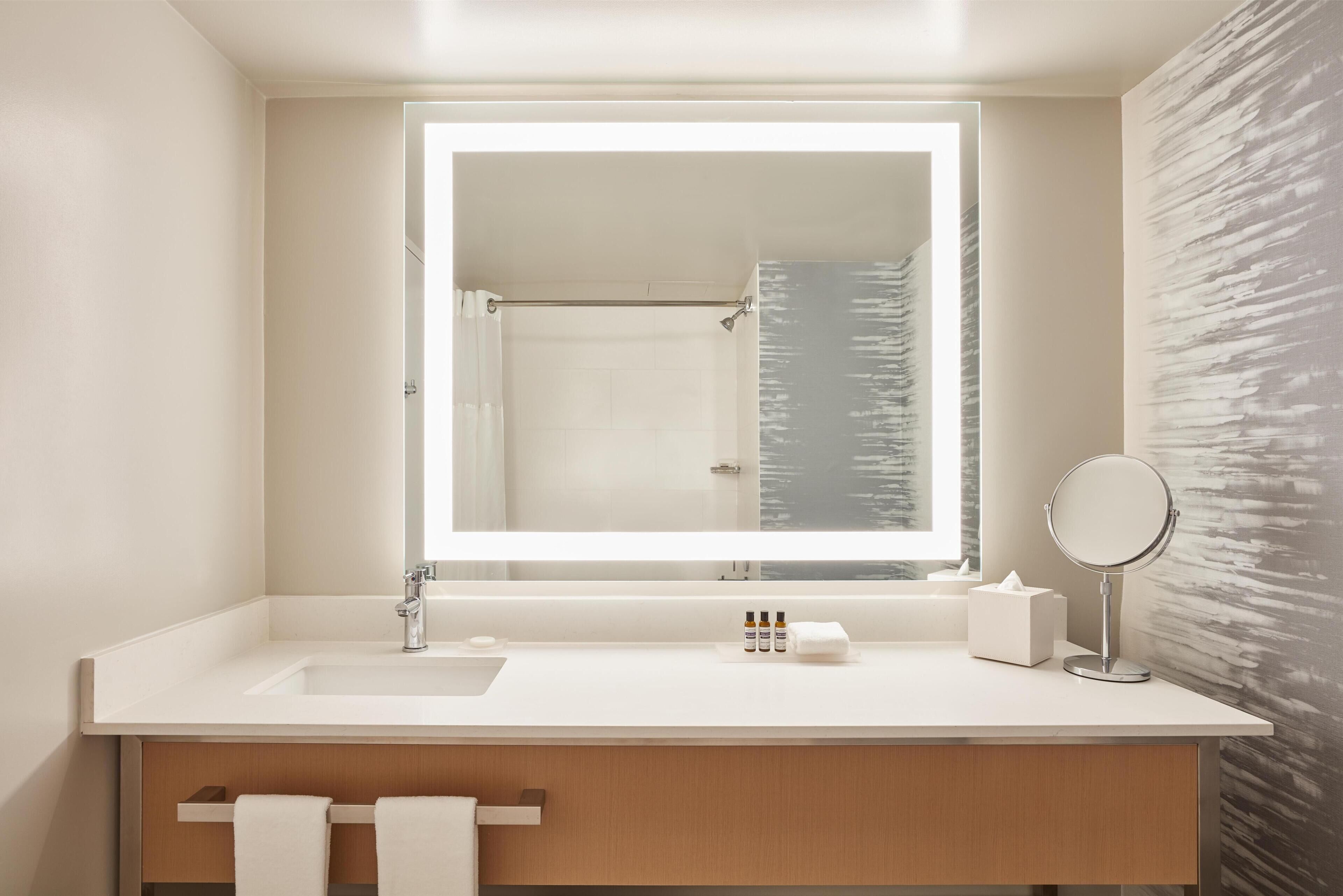 A modern bathroom with a large mirror, a sink, and a shower visible in the background.