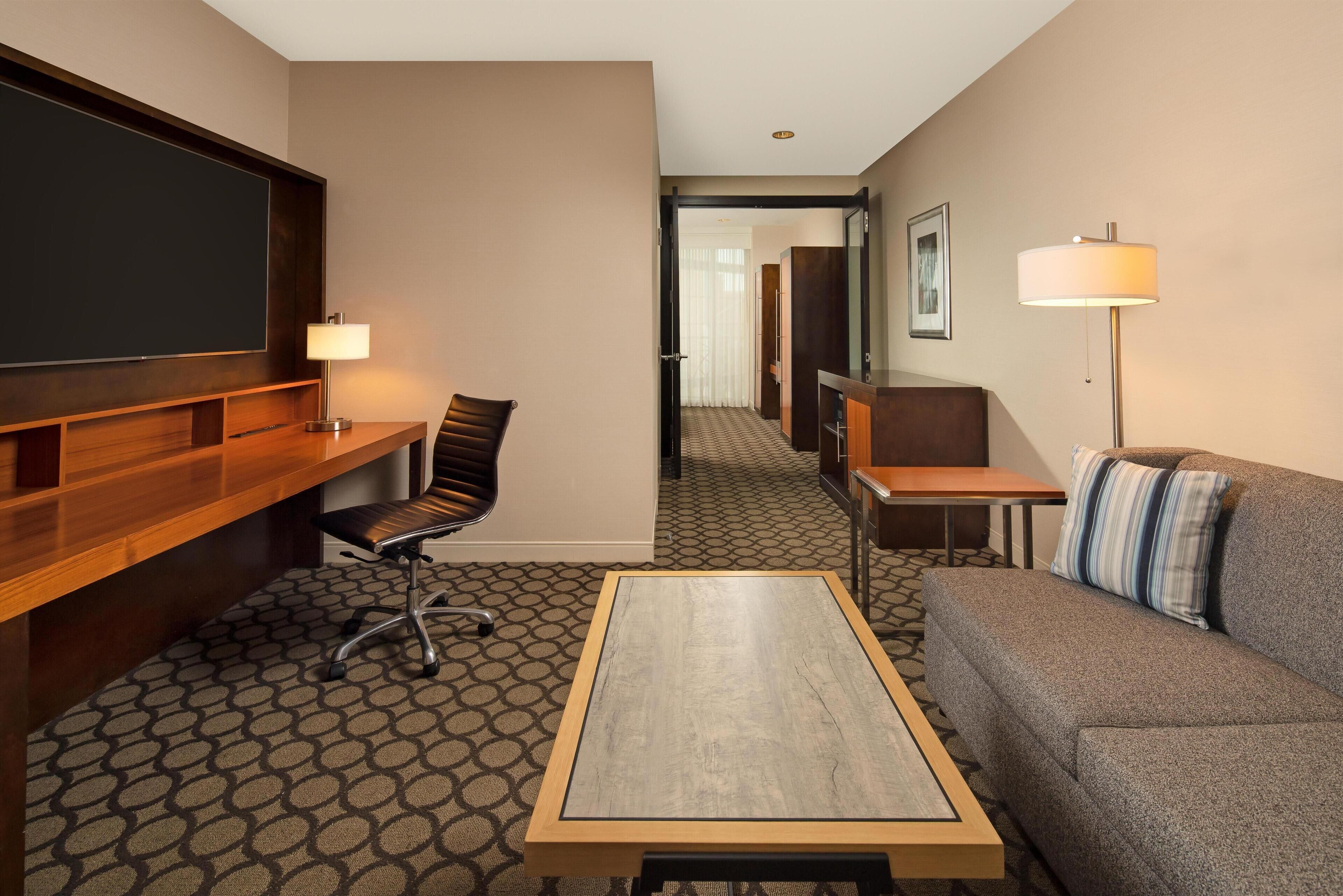 A hotel room with a desk, chair, sofa, and a television.