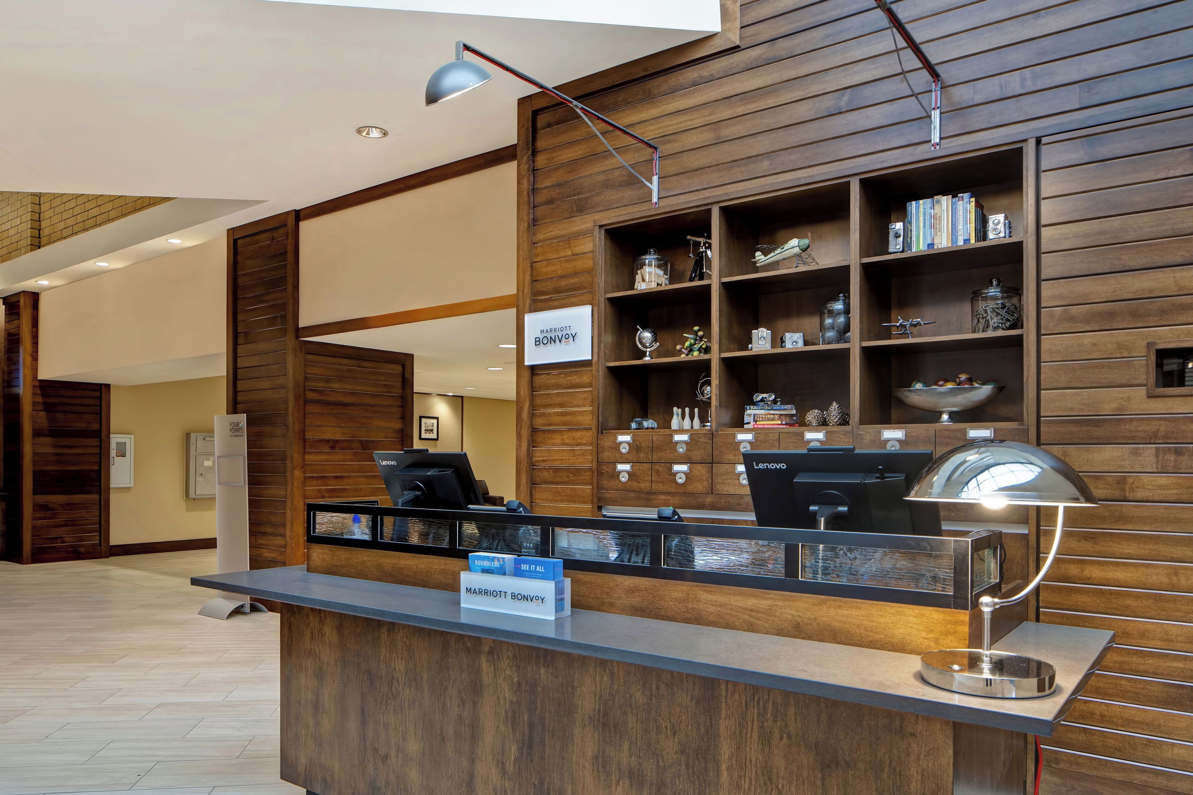 A hotel reception desk with a wooden panel wall, a computer, and a desk lamp.