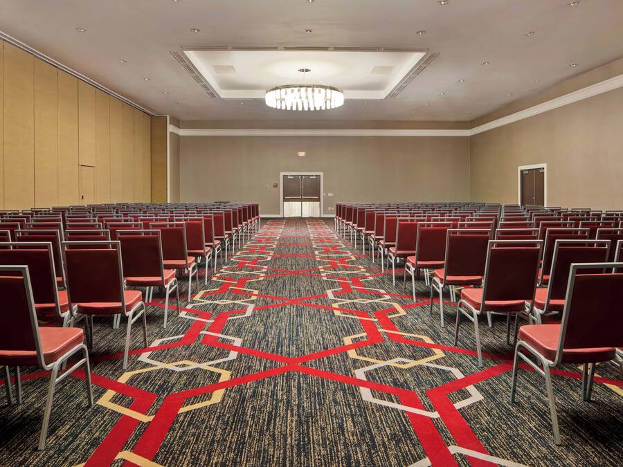 A conference room with rows of chairs, a patterned carpet, and a ceiling light fixture.