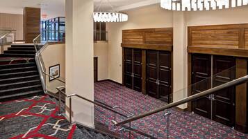 Een hotelhal met een trap, een getextureerd tapijt, houten kasten en een moderne kroonluchter.