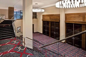 Vestíbulo de hotel con una escalera, alfombra estampada, taquillas de madera y una lámpara de araña moderna.