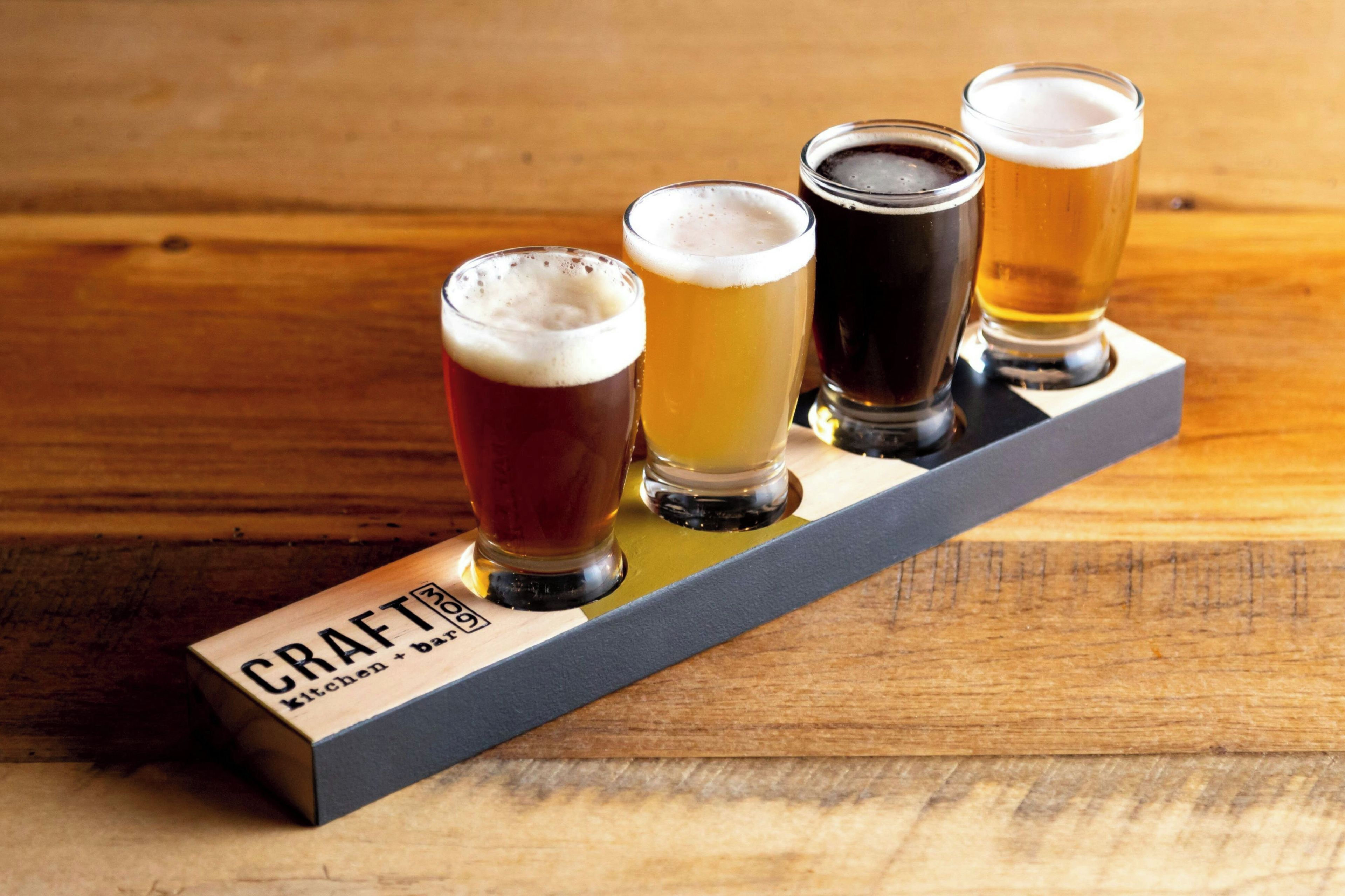 A wooden bar with five glasses of beer in a row.