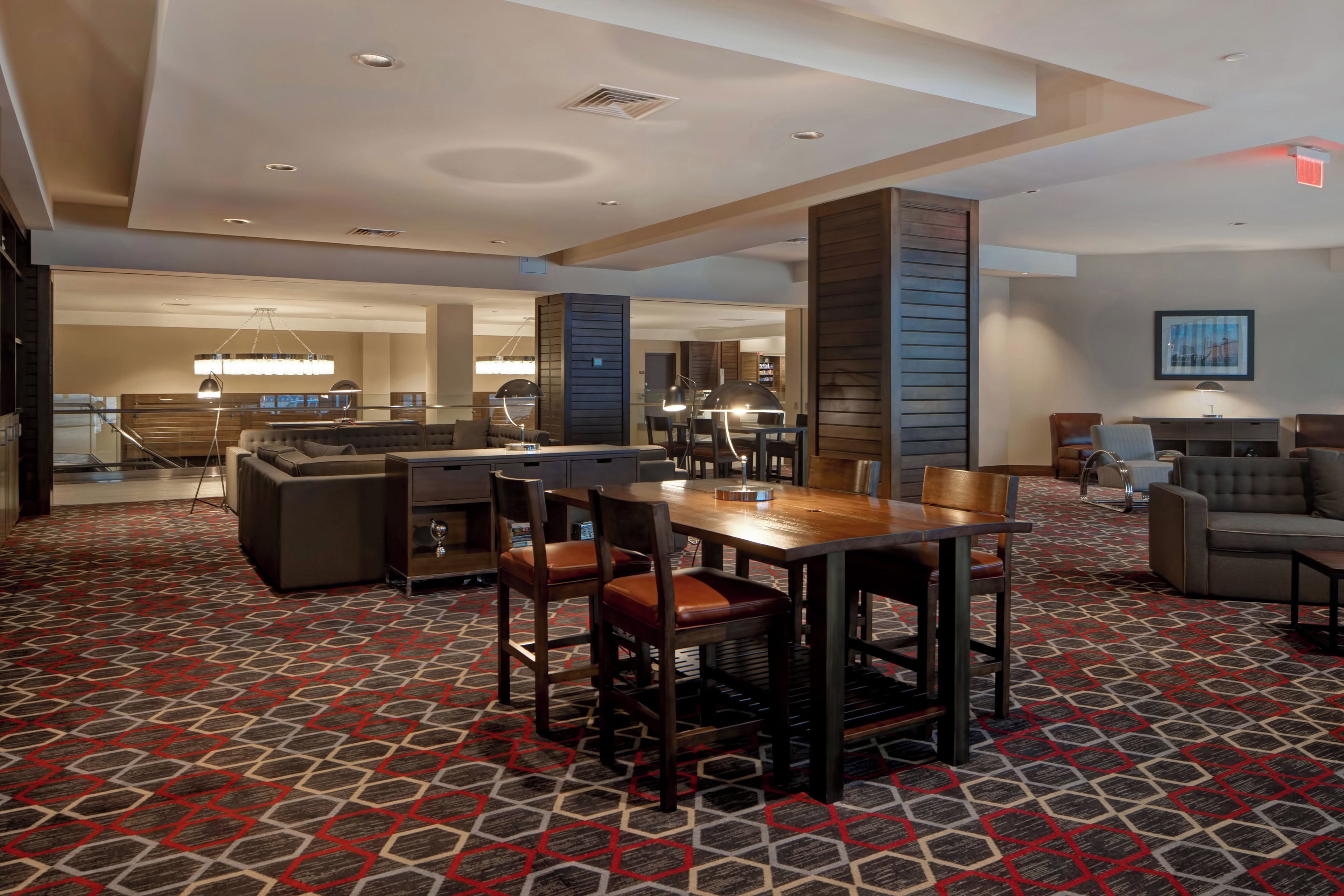 A hotel lobby with a dining area, sofas, and a patterned carpet.