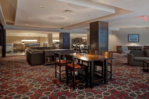 Hall d'albergo con zona ristorazione, divani e tappeto a motivi decorativi.