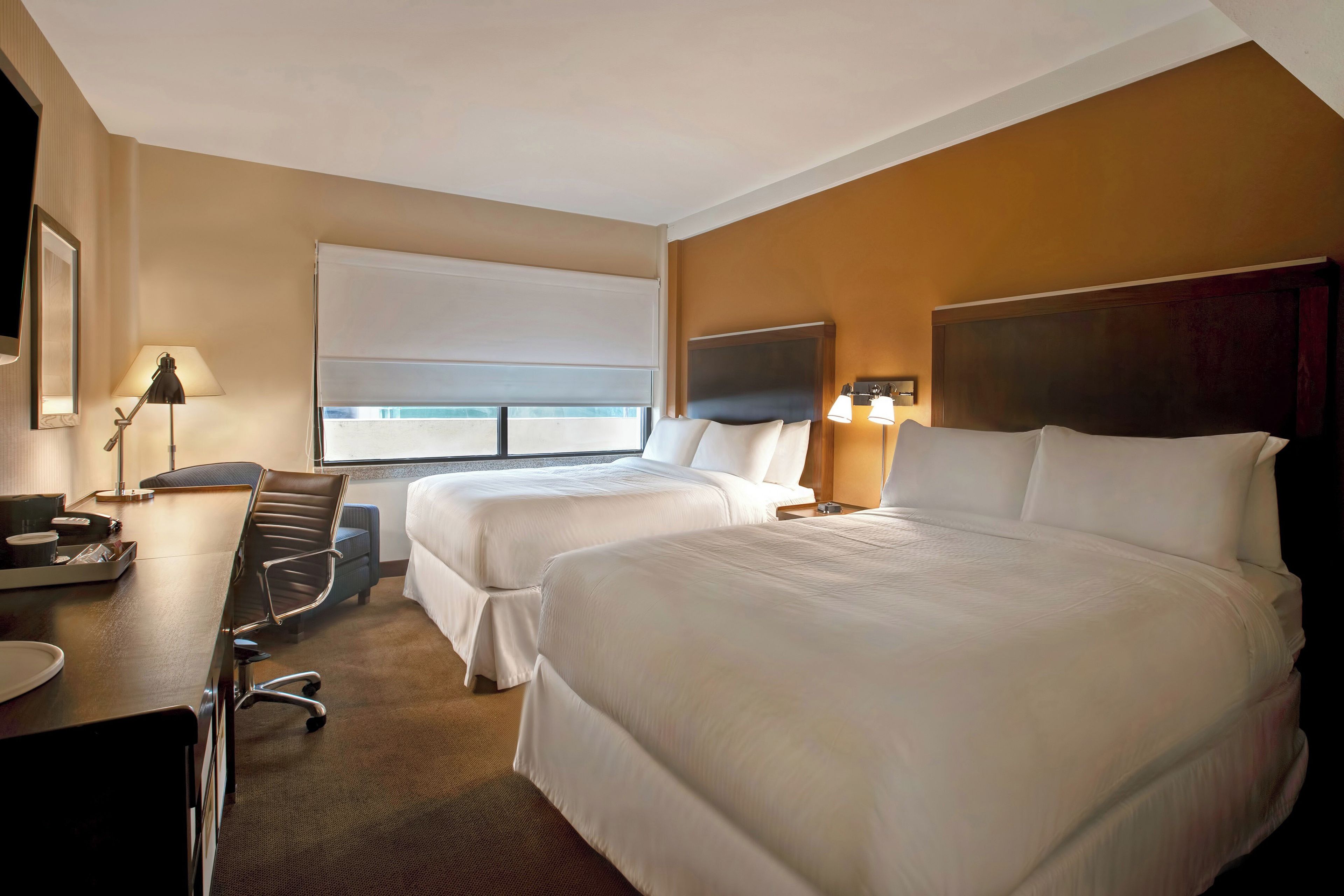 Habitación de hotel con dos camas, un escritorio, una silla, un televisor y ventana con vistas.