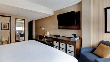 A hotel room with a large bed, a desk with a chair, a flat-screen TV mounted on the wall, and a sofa.