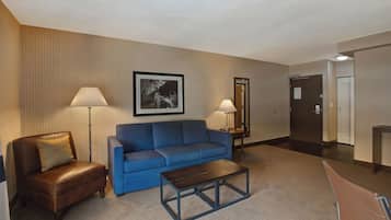 A hotel room with a brown leather chair, a blue sofa, a small wooden coffee table, and two floor lamps.