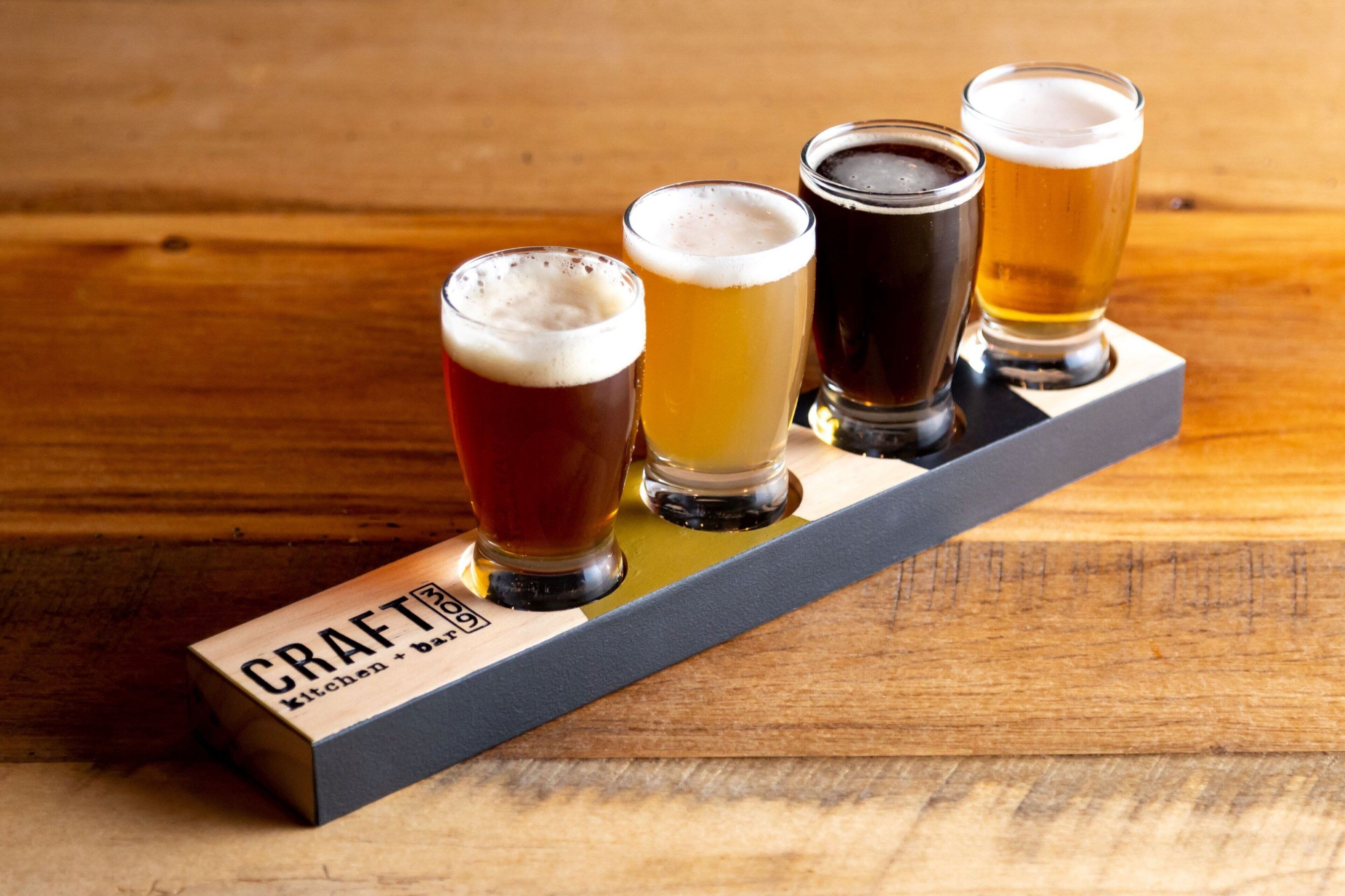 A wooden bar counter with five glasses of beer.