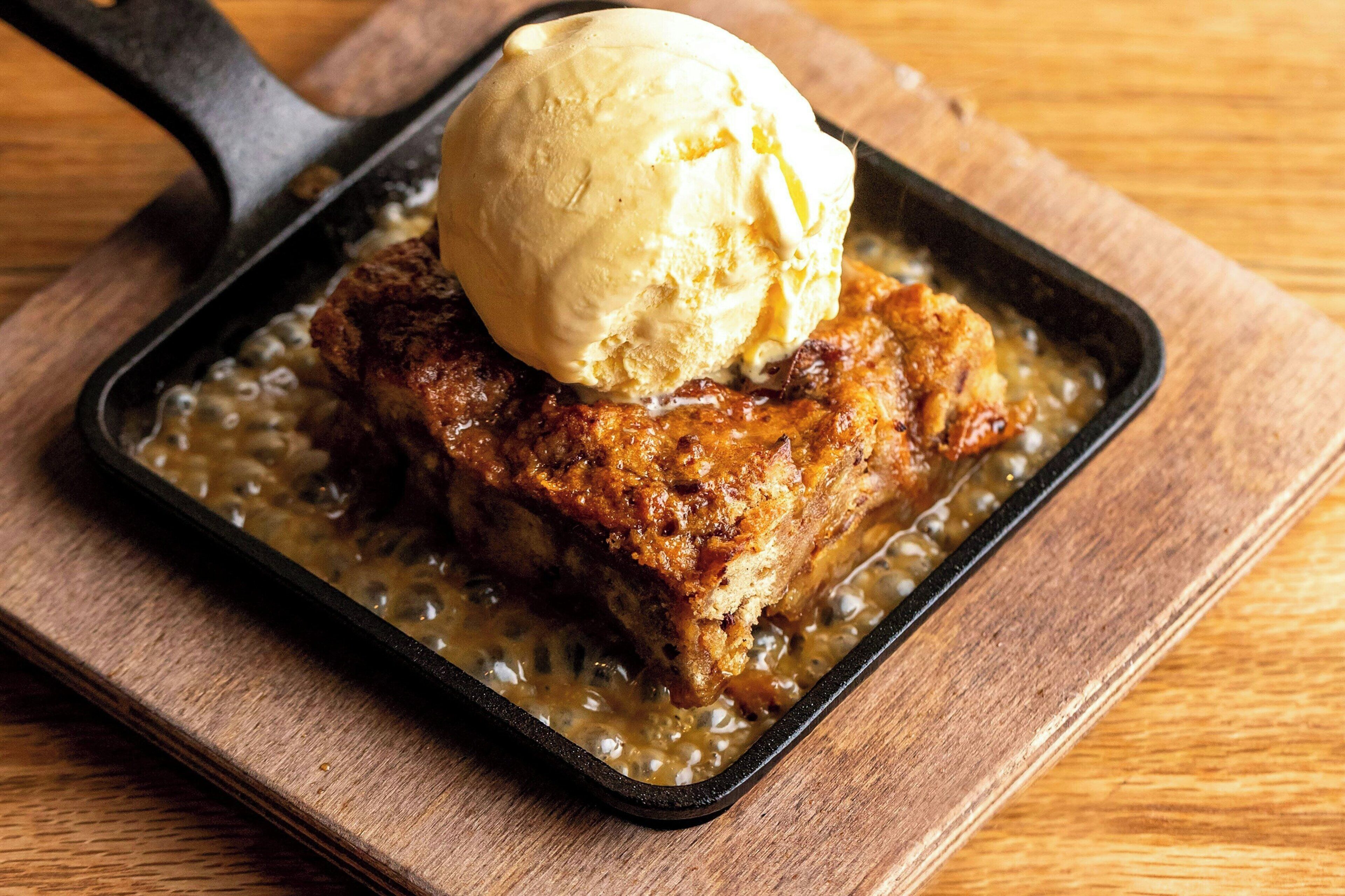 A skillet with a piece of breaded meat and a scoop of ice cream on a wooden surface.