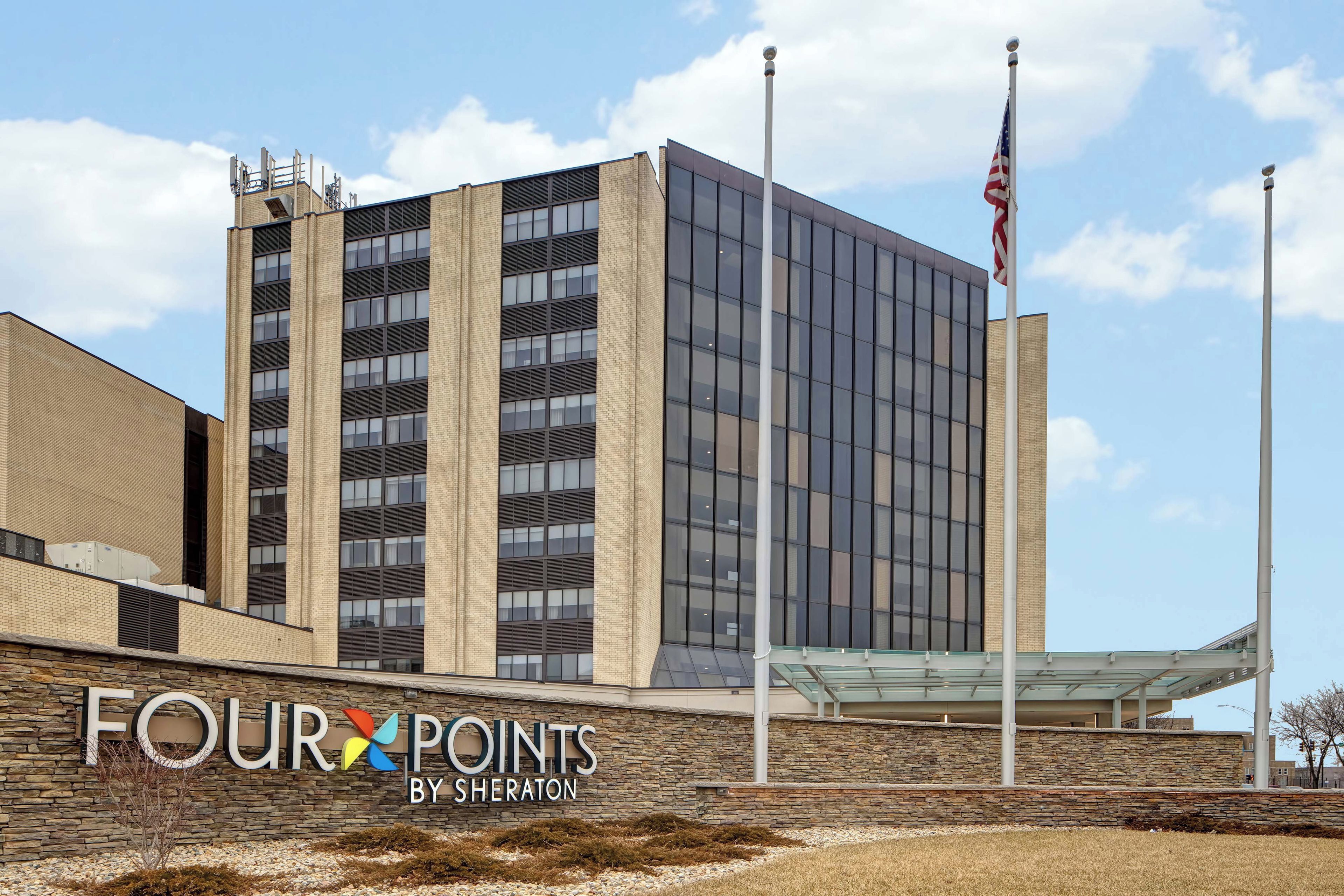 A modern building with a glass facade, a stone wall with signage, and an American flag.