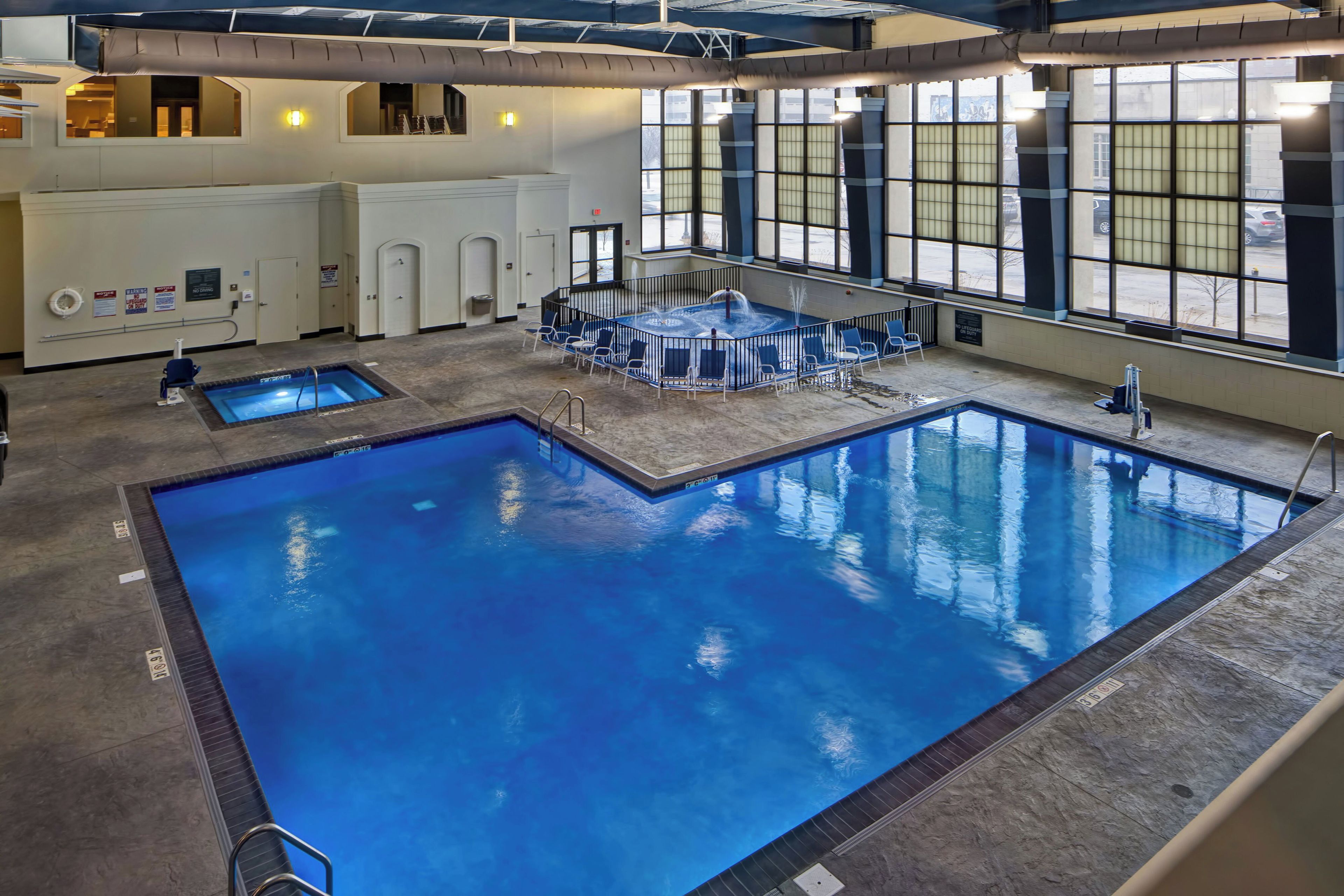 A large indoor swimming pool with multiple lanes, a lounge area with chairs, and a view of the outside through large windows.