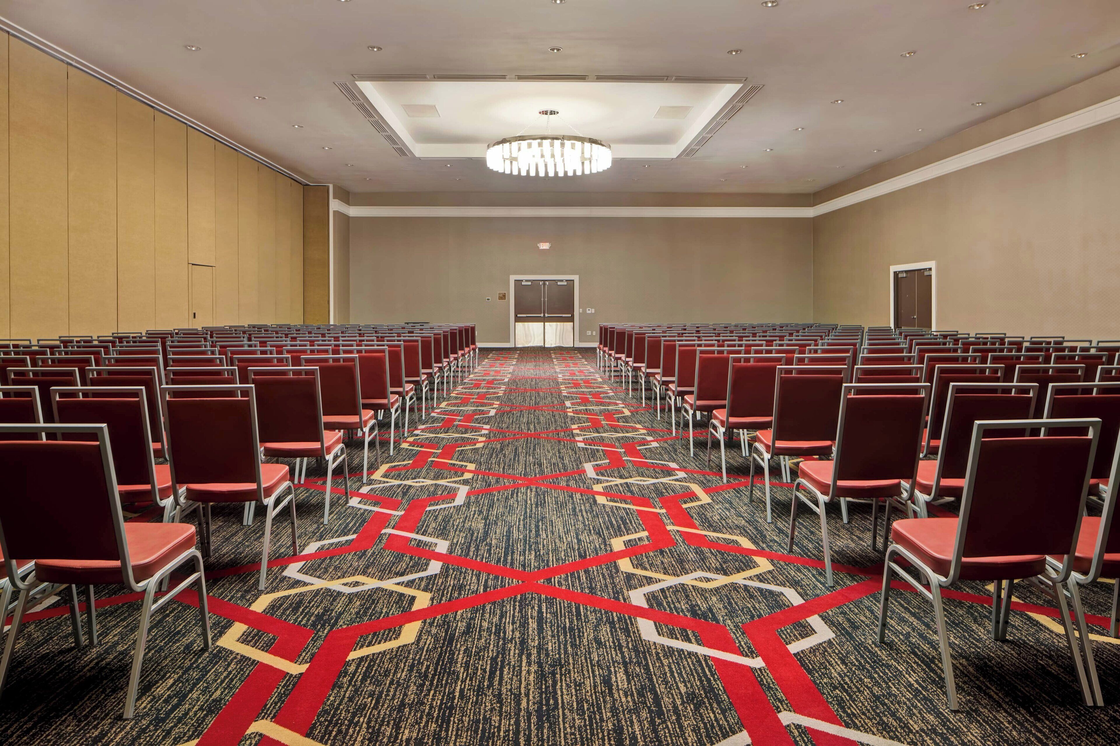 Une salle de conférence avec des rangées de chaises rouges, une moquette à motifs et un grand lustre.