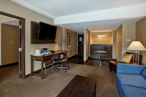 A hotel room with a flat-screen TV mounted on the wall, a desk with a chair, a sofa, a coffee table, and a lamp. - Four Points By Sheraton Peoria (Peoria)