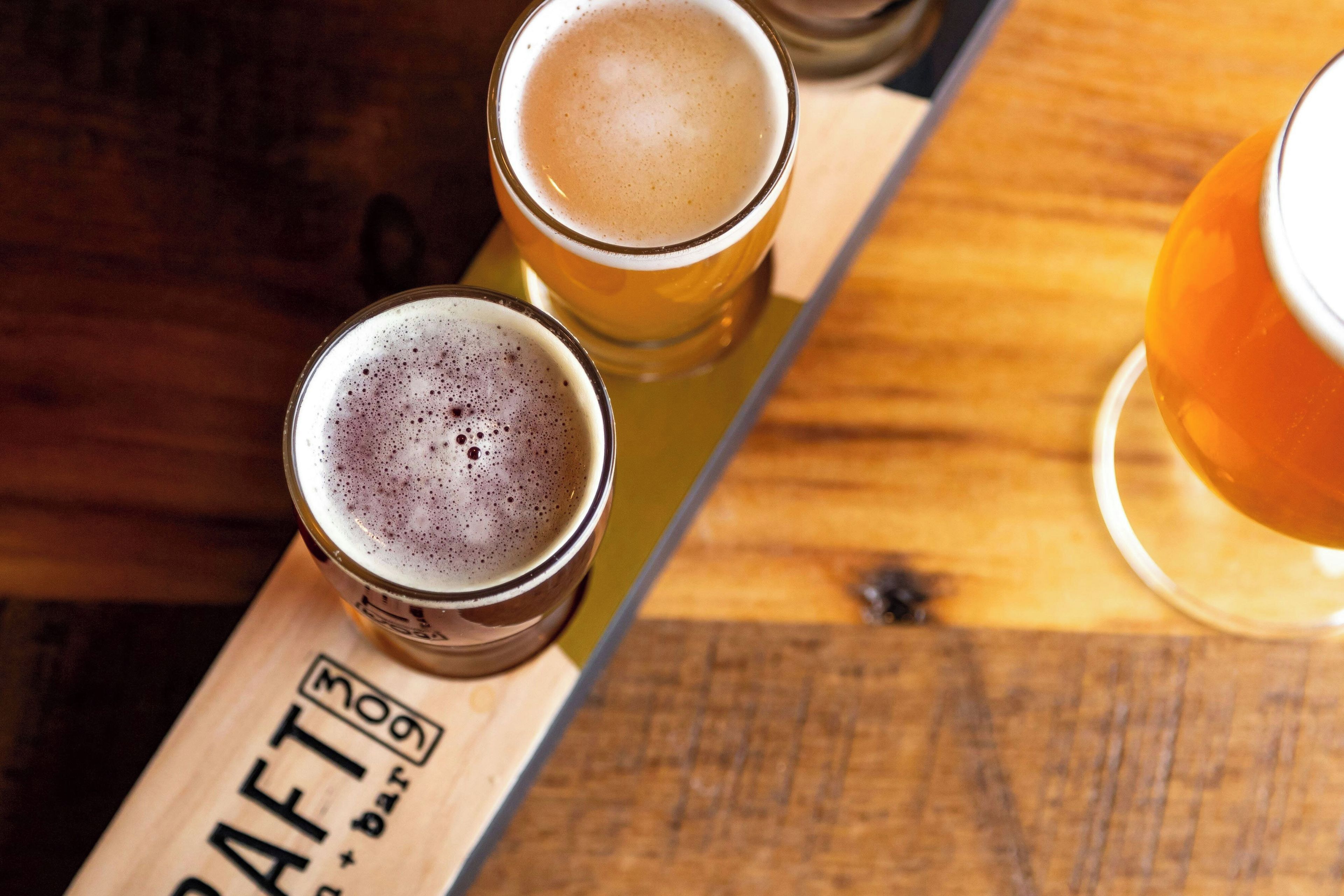 Tres vasos de cerveza sobre una bandeja de madera con un logotipo.