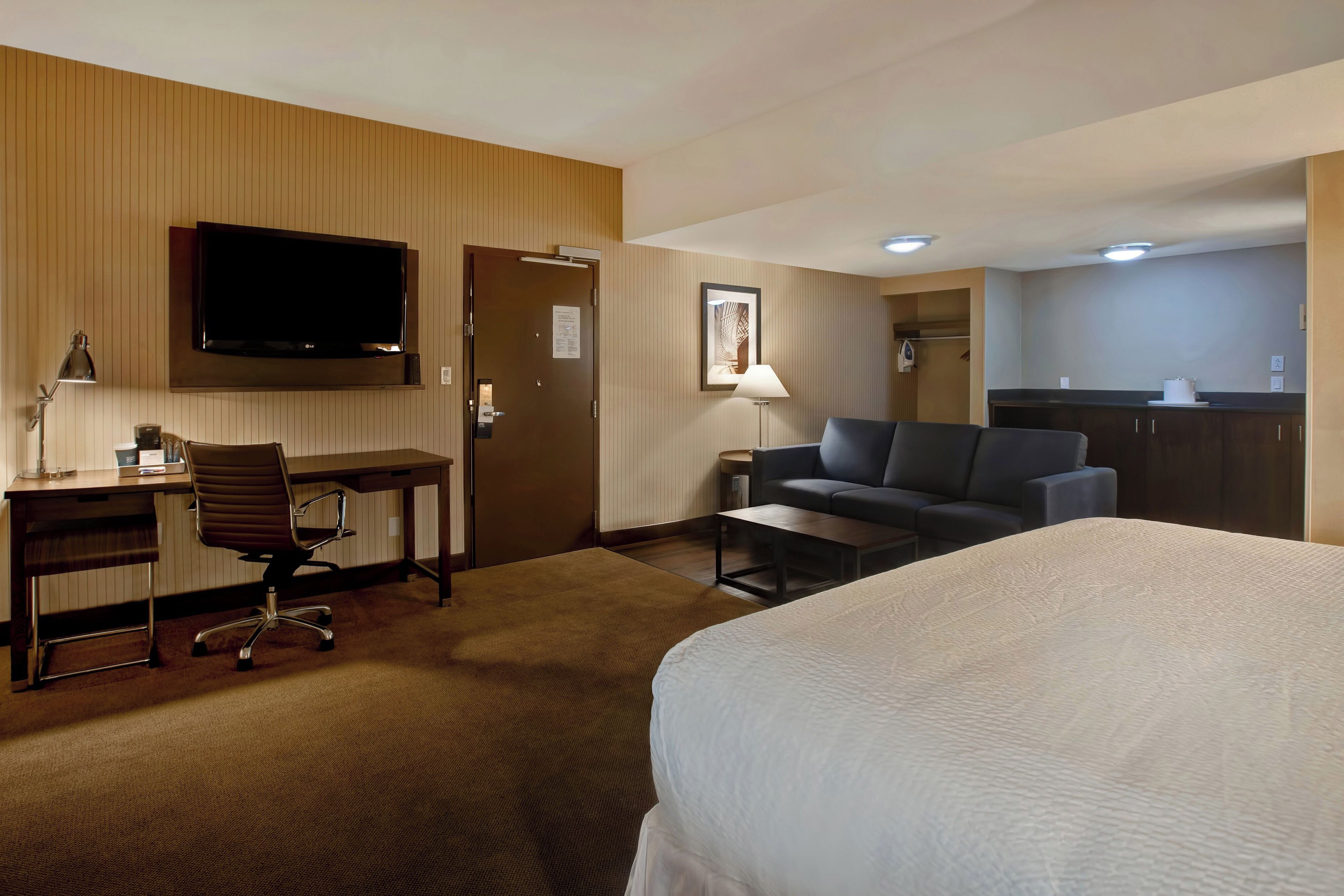 A hotel room with a bed, a desk with a chair, a sofa, a television, and a kitchenette.