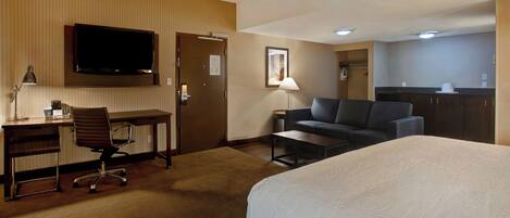 A hotel room with a bed, a desk with a chair, a sofa, a television, and a kitchenette.