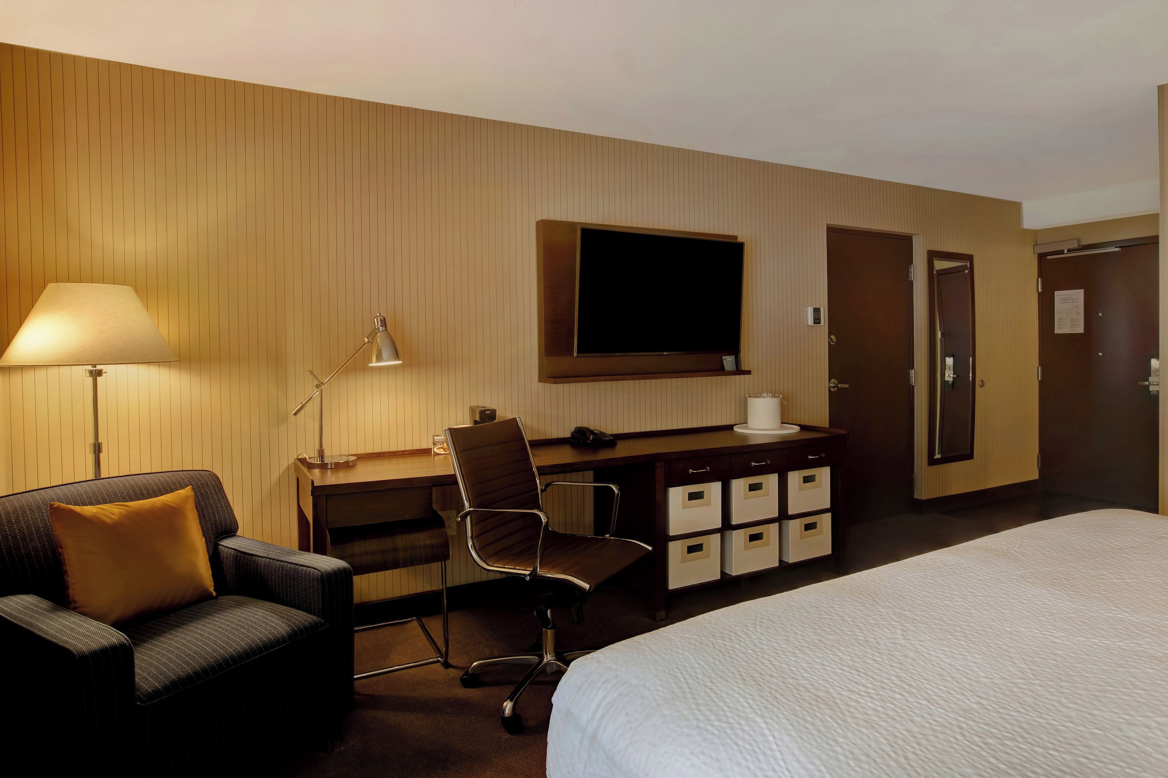 Een hotelkamer met een bed, een bureau met een stoel, een televisie, een lamp en een kledingkast.