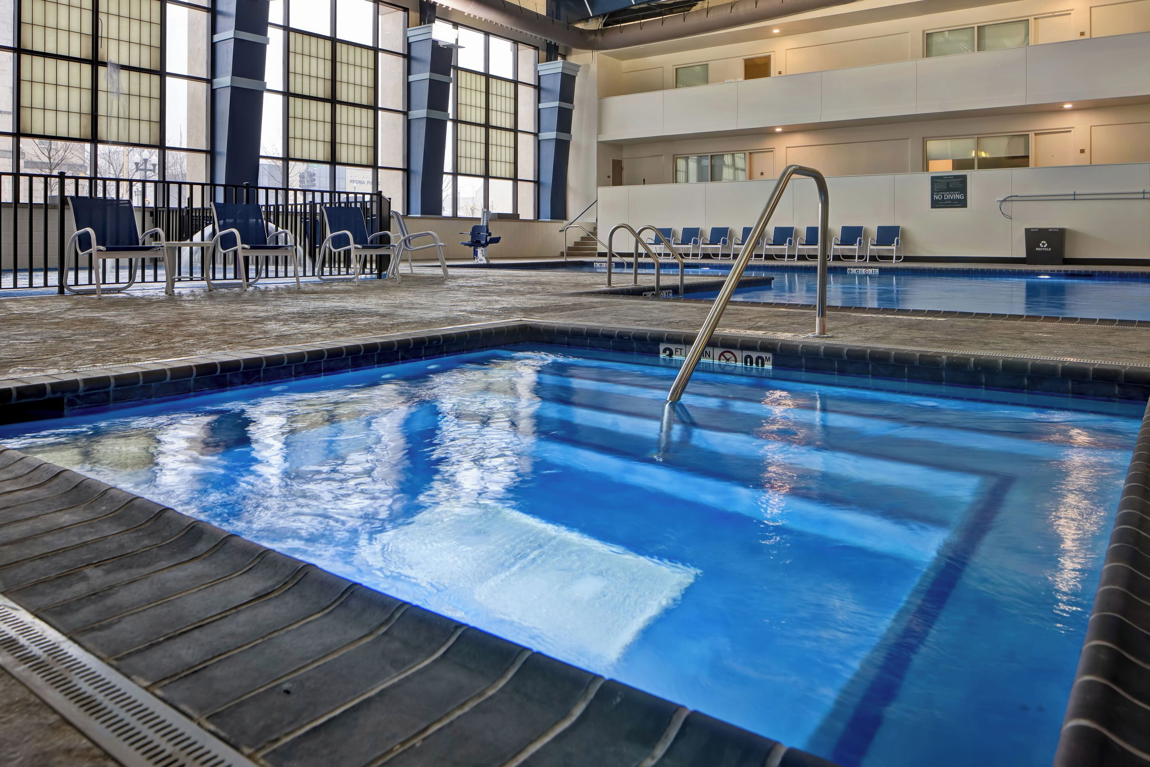 Una piscina interior con agua cristalina, un trampolín y sillones de descanso.