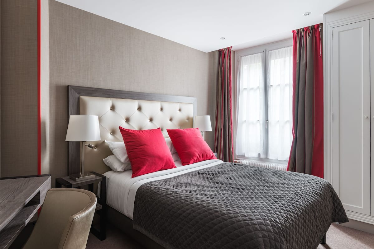 A hotel room with a large bed, two bedside lamps, a desk, and a wardrobe.
