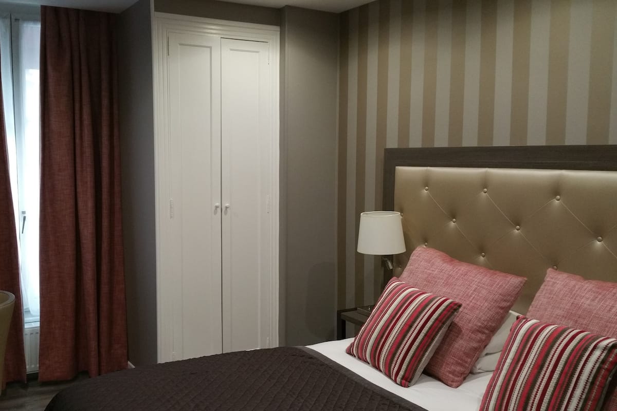 A hotel room with a bed, a desk, a chair, a wardrobe, and a striped wall.