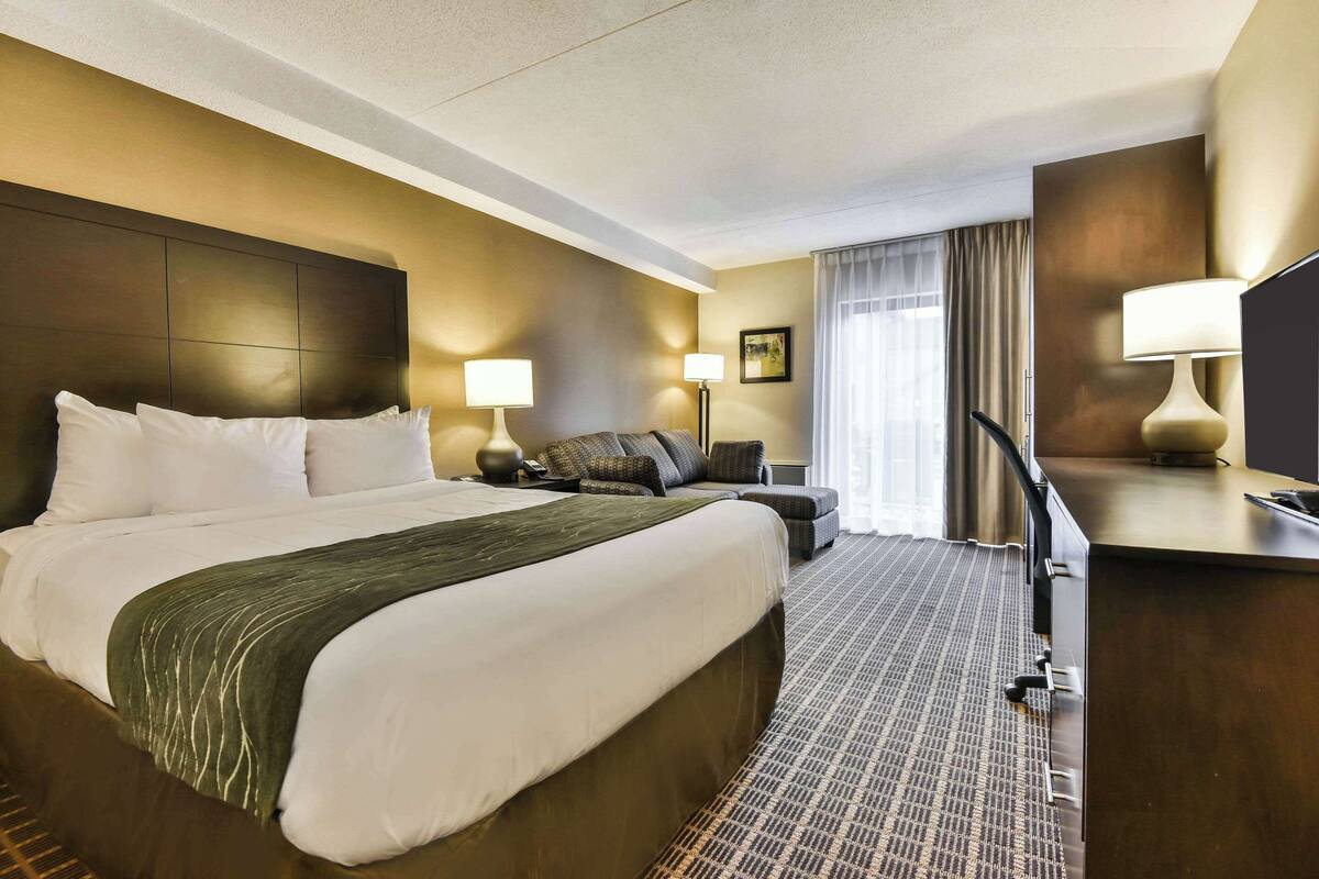A hotel room with a large bed, a desk, a chair, and a TV.