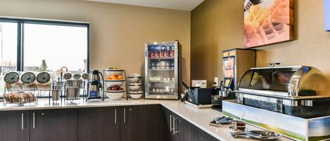 Una barra de desayuno con refrigerador, cafetera y exhibición de alimentos.