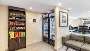A hotel lobby with a snack shelf, beverage refrigerator, and a seating area.